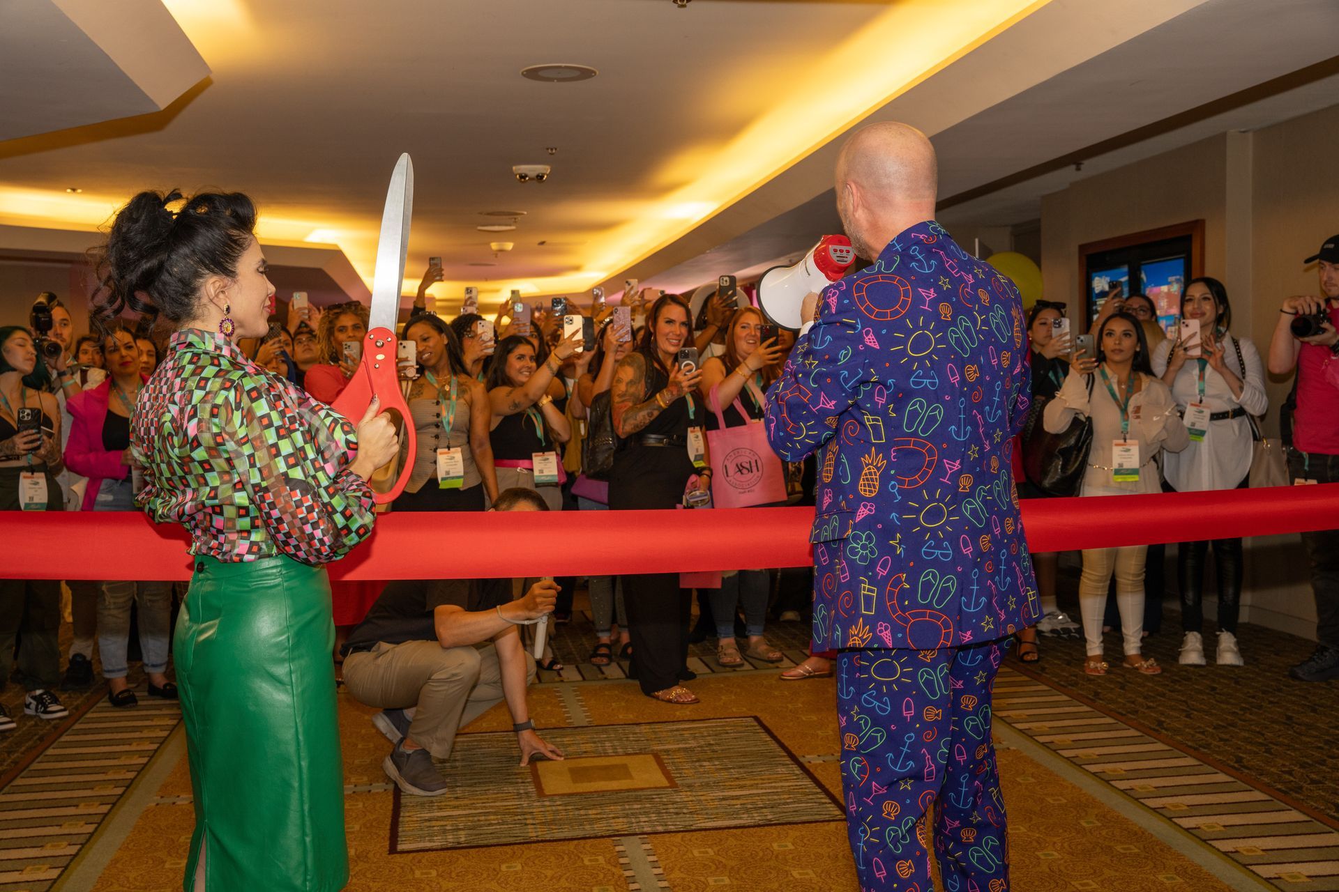 A man and a woman are cutting a red ribbon in front of a crowd.