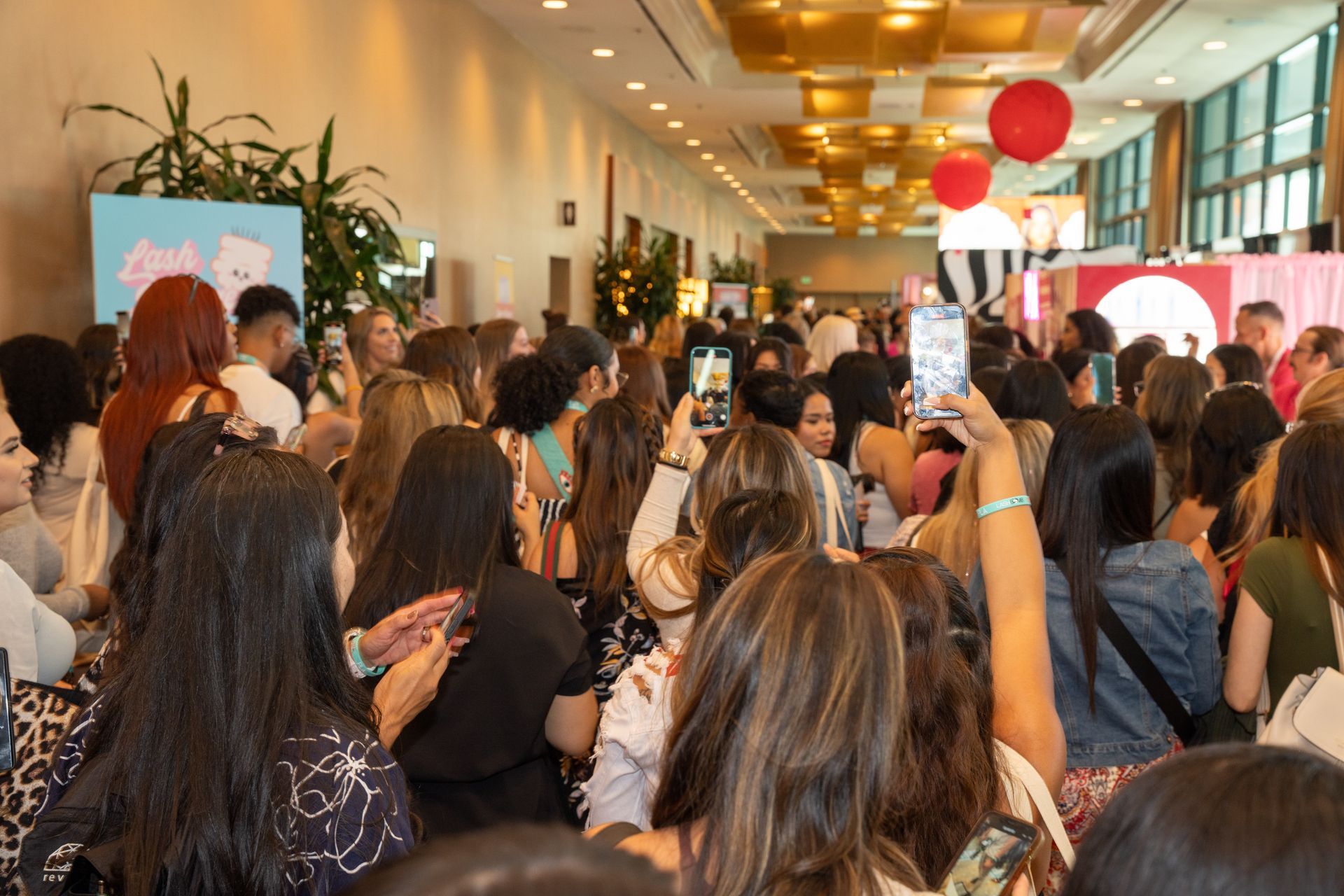A large group of people are standing in a room taking pictures with their phones.