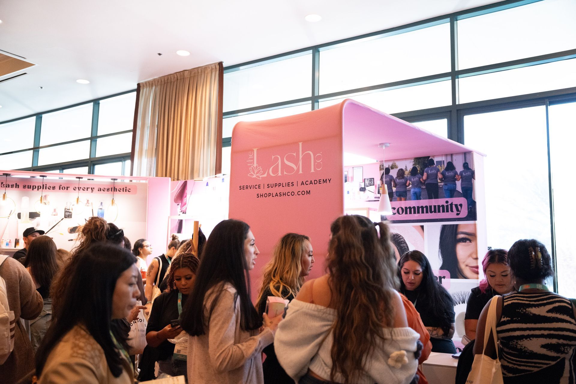 A group of women are standing in front of a pink booth at a convention.