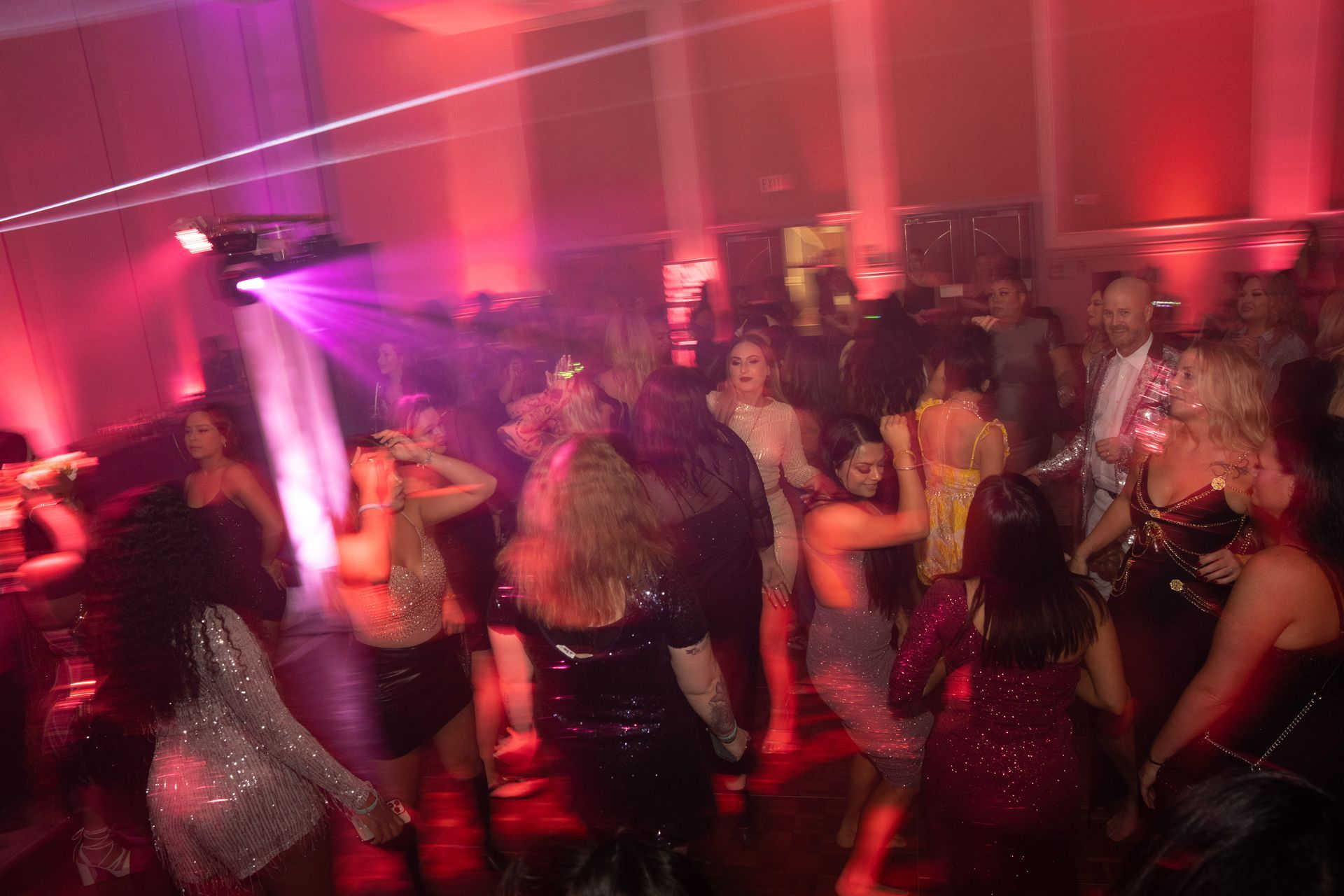 A large group of people are dancing at a party in a dark room.