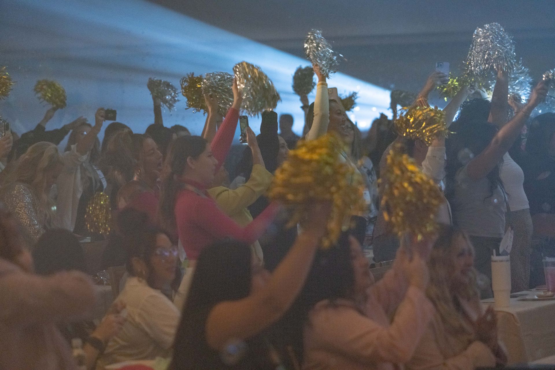 A crowd of people are holding pom poms in the air at a party.
