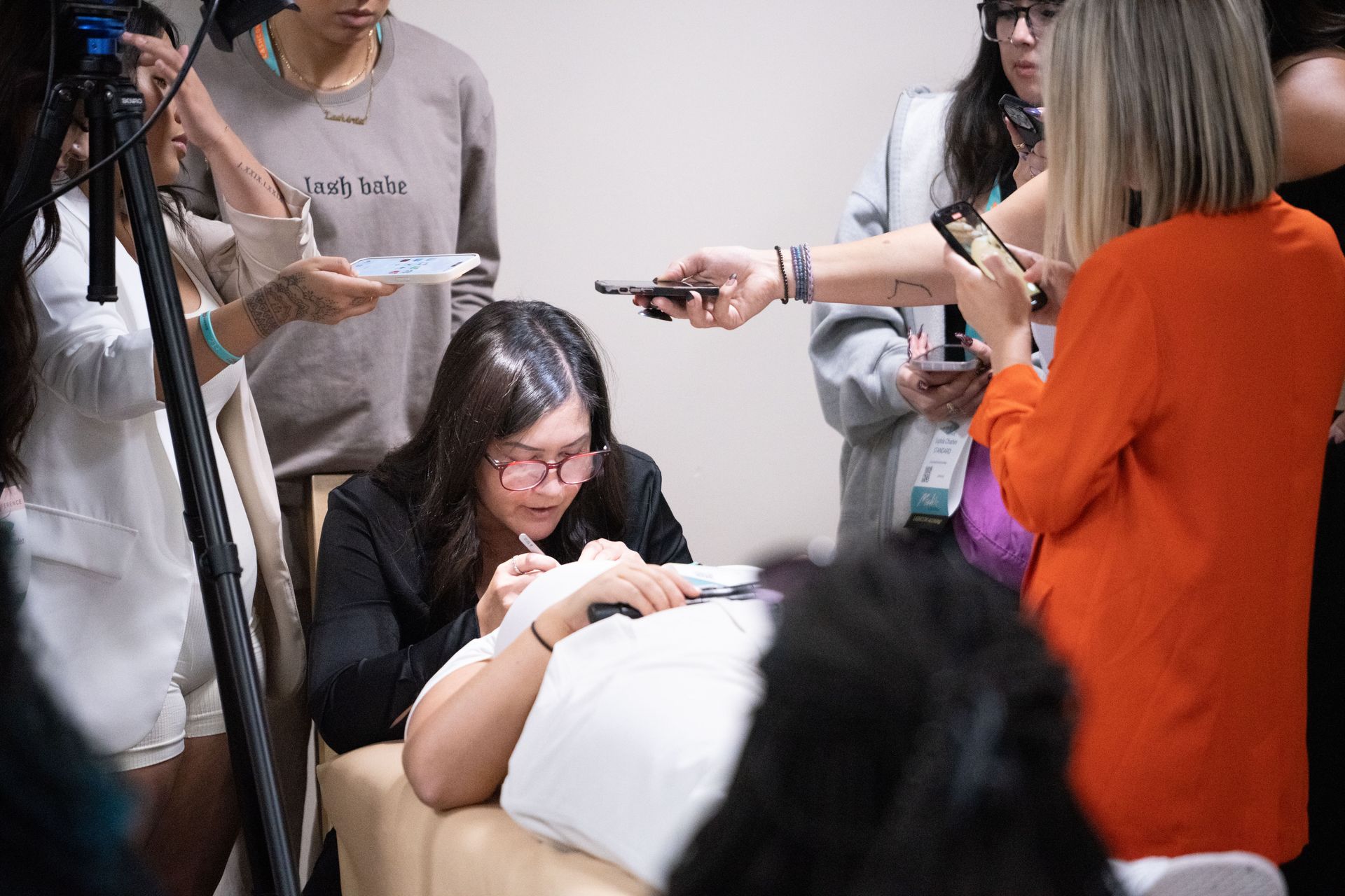 A group of people are standing around a woman laying on a bed.