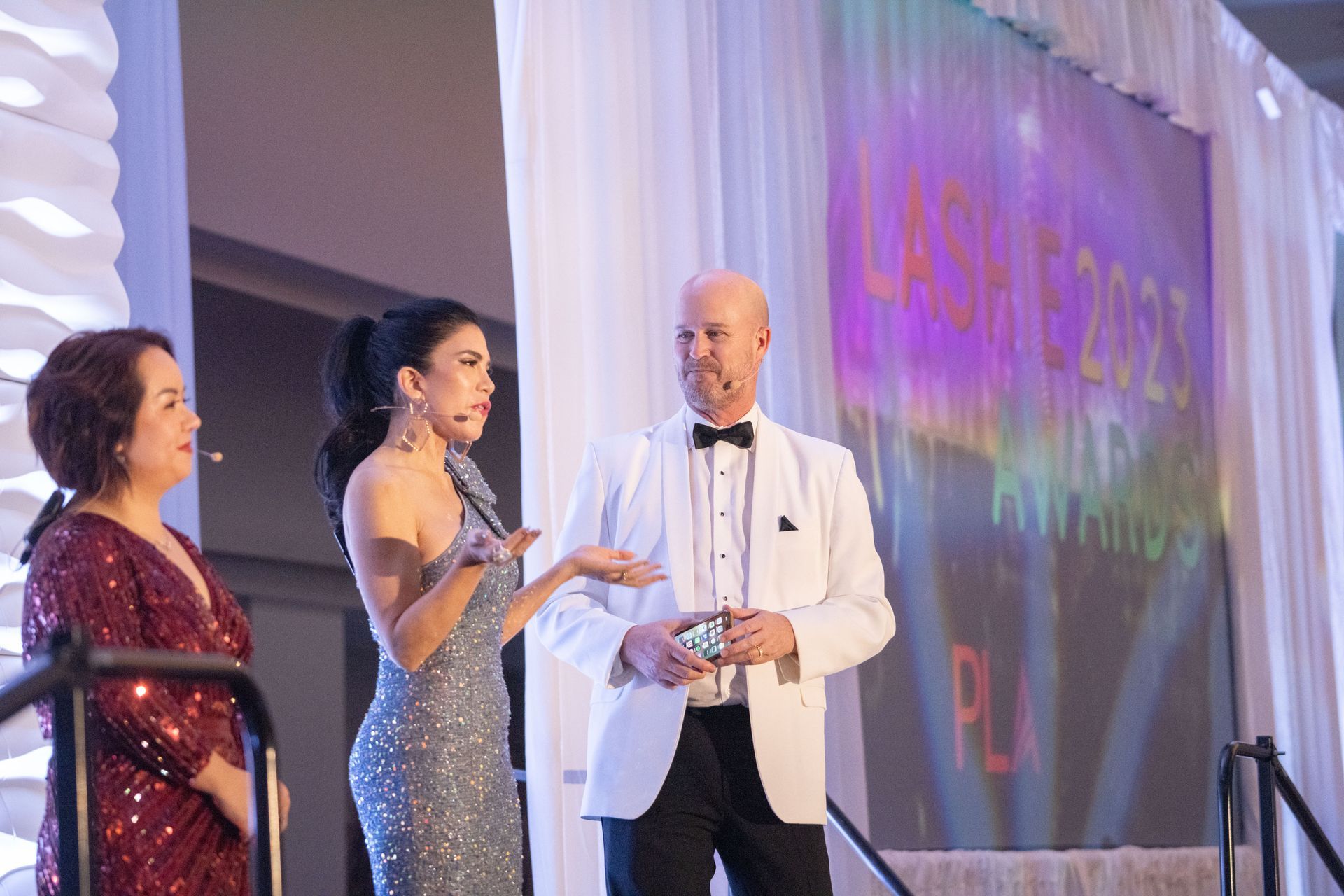 A man in a tuxedo is standing next to two women on a stage.
