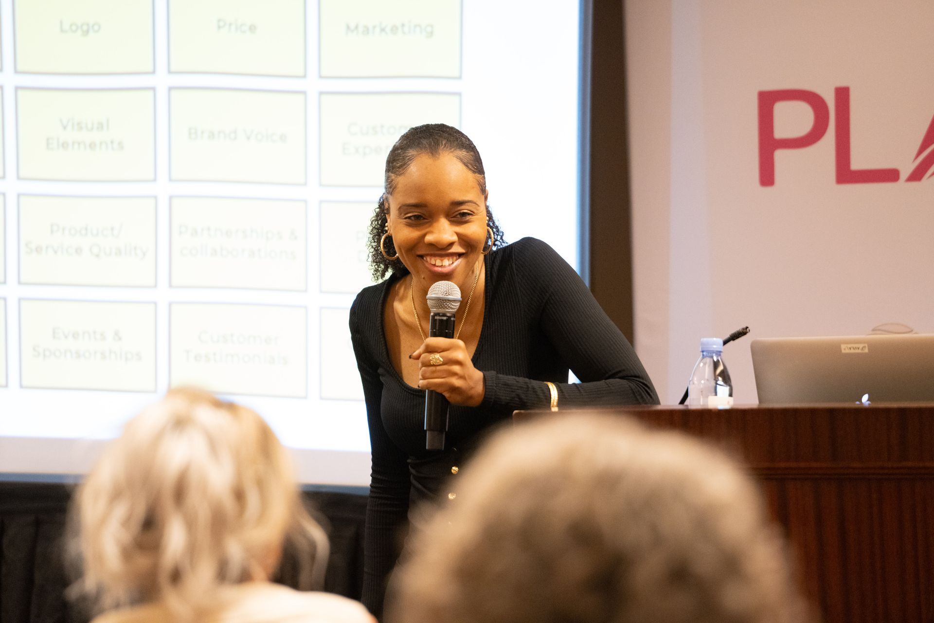 A woman is holding a microphone and smiling while giving a presentation.