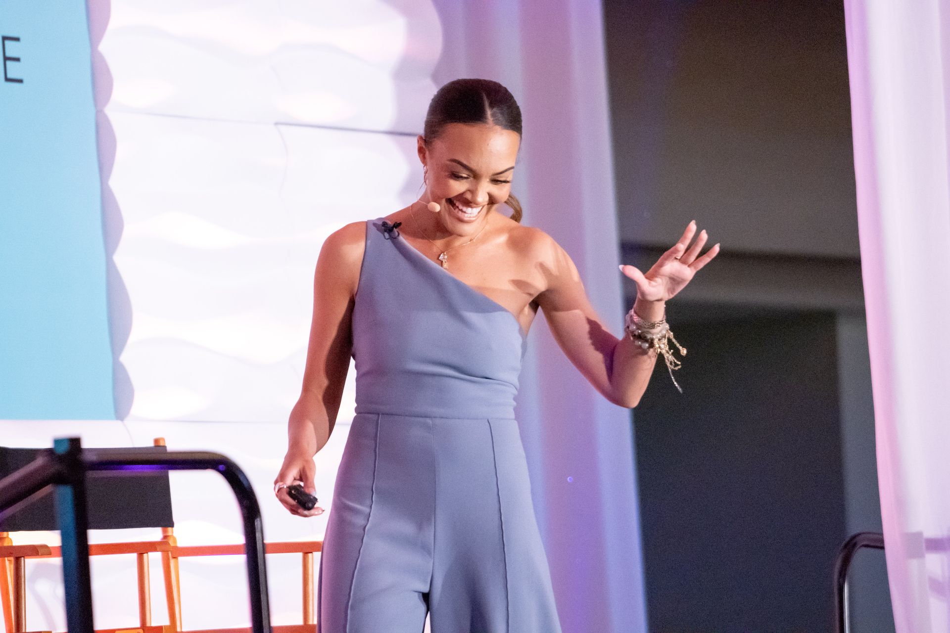 A woman in a blue jumpsuit is standing on a stage holding a microphone.