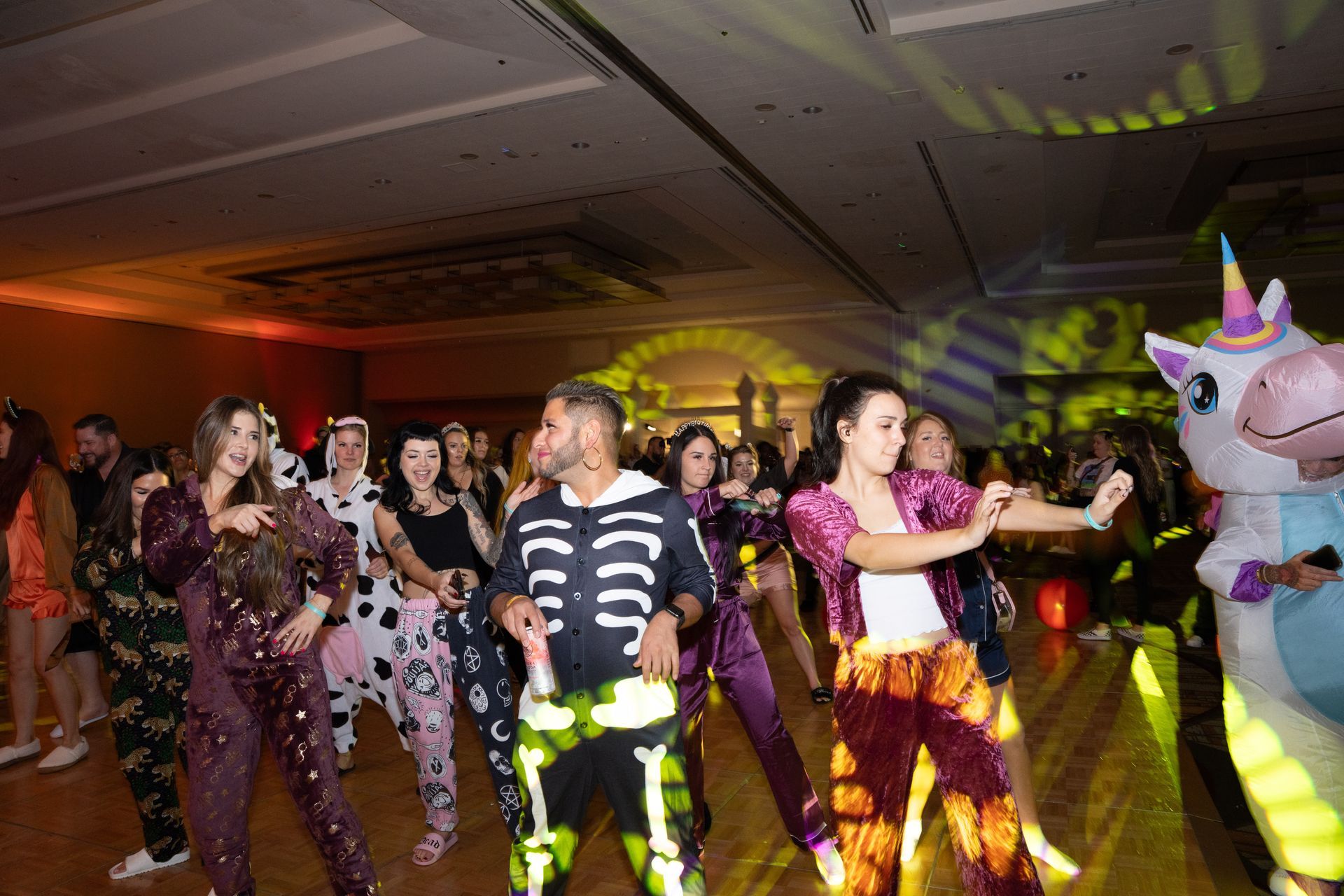 A group of people are dancing in a room with a unicorn mascot.