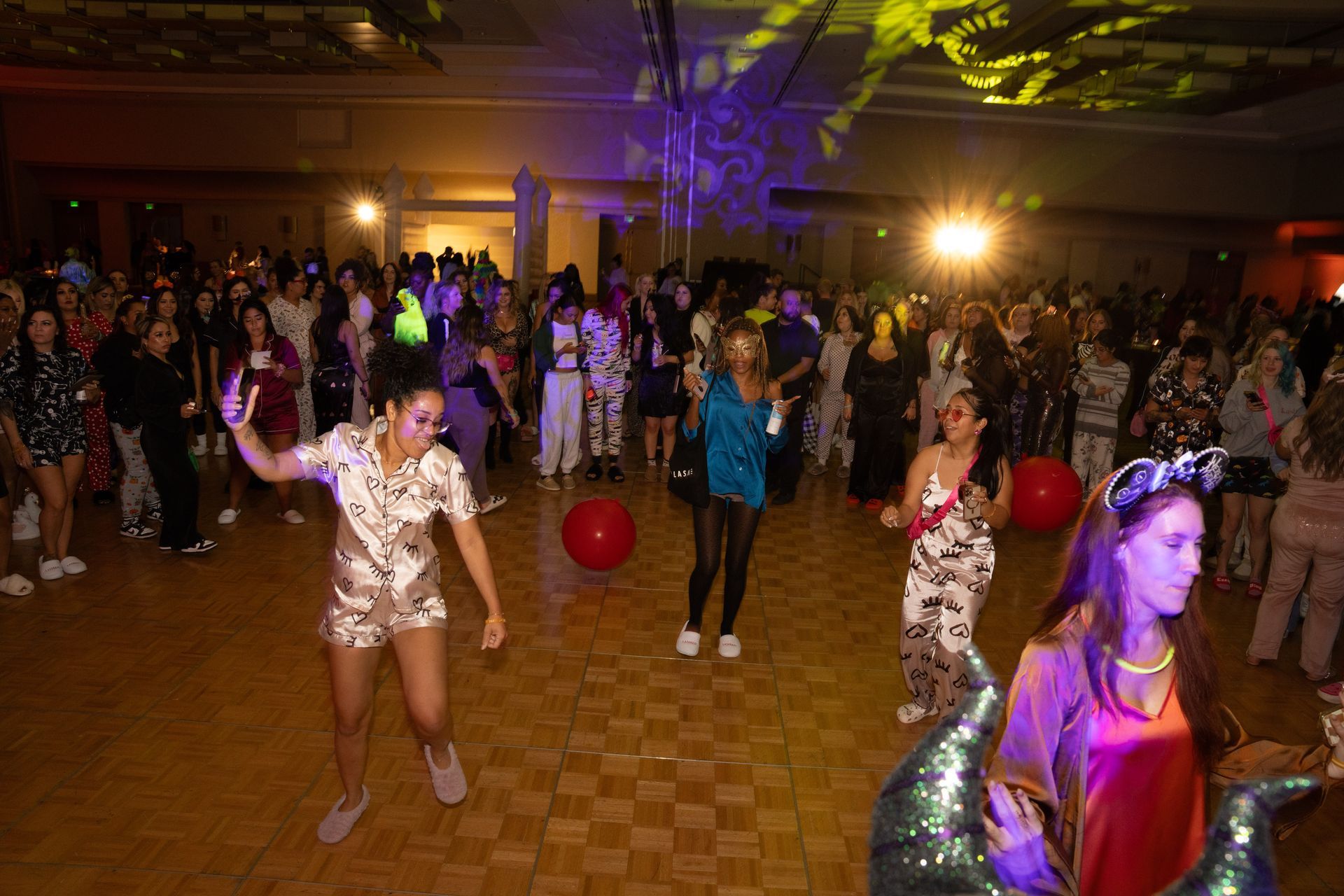 A group of people are dancing in a large room at a party.