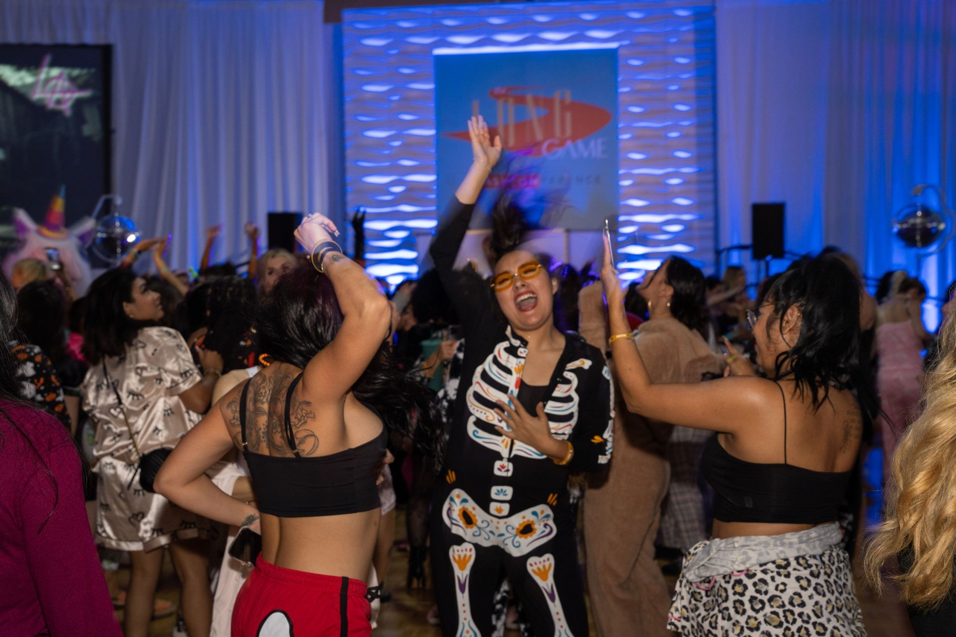 A woman in a skeleton costume is dancing in a crowd of people at a party.