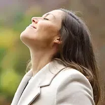 A woman in a white coat is looking up with her eyes closed.