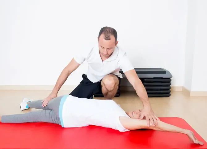 A man is helping a woman stretch her legs on a red mat