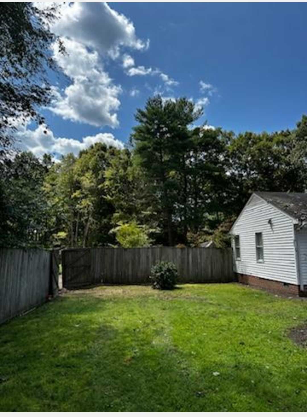 A backyard with a white house and a wooden fence