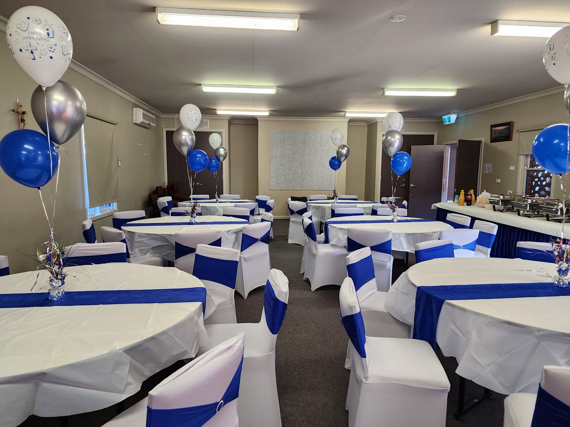 A large room with tables and chairs decorated for a party with blue and silver balloons.