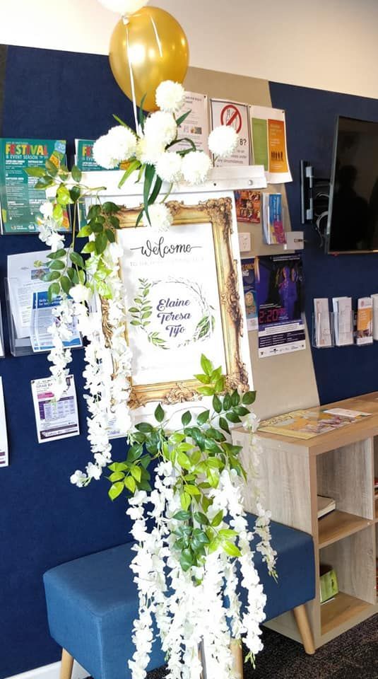 A welcome sign with flowers and balloons in a room.
