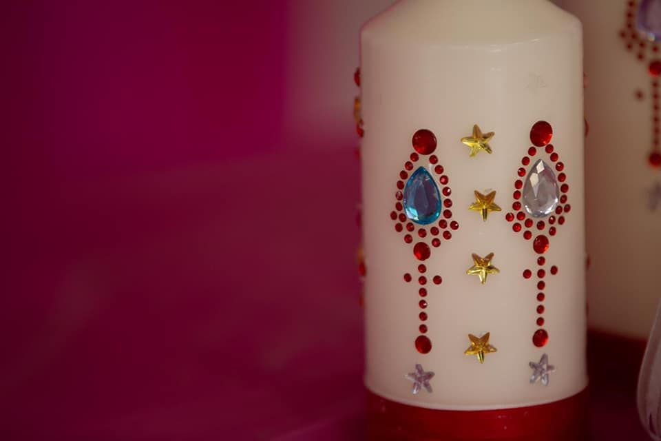 A white candle with rhinestones and stars on it is sitting on a pink table.