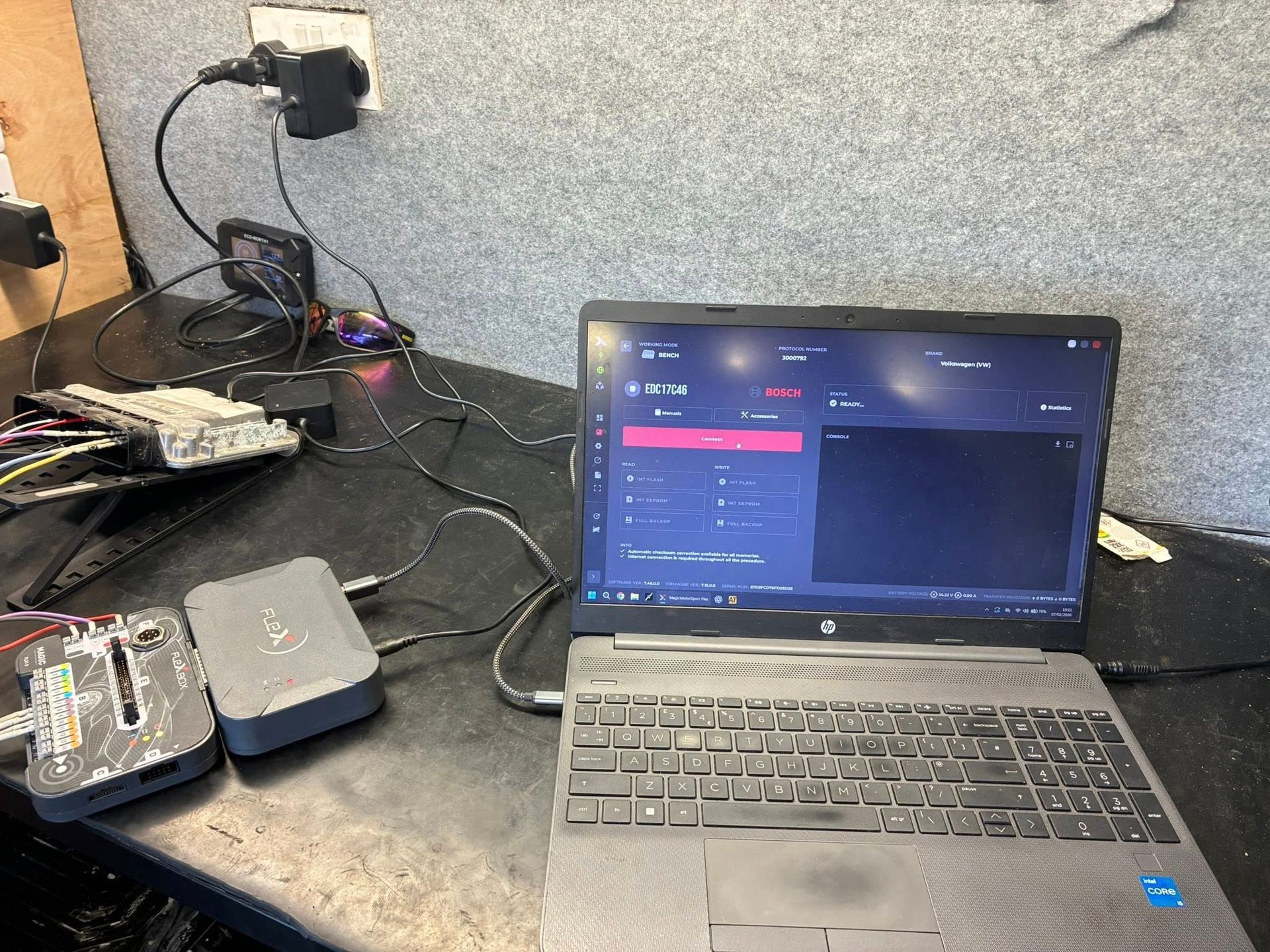 Laptop with software, connected to devices on a workbench. Black, gray, and silver components. Wires and electrical connections.