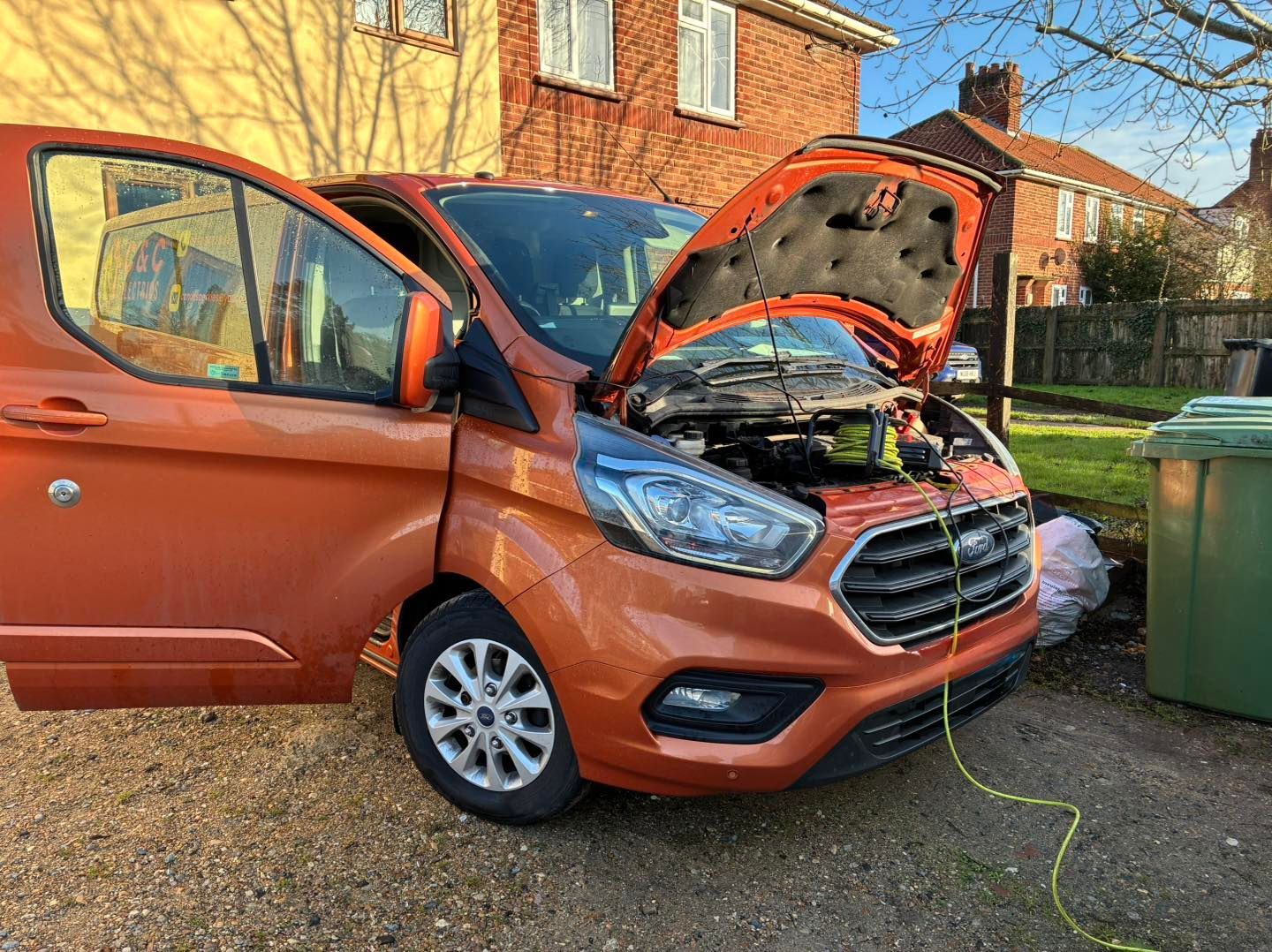 Orange van with open hood and door parked outside a house, appears to be undergoing maintenance.