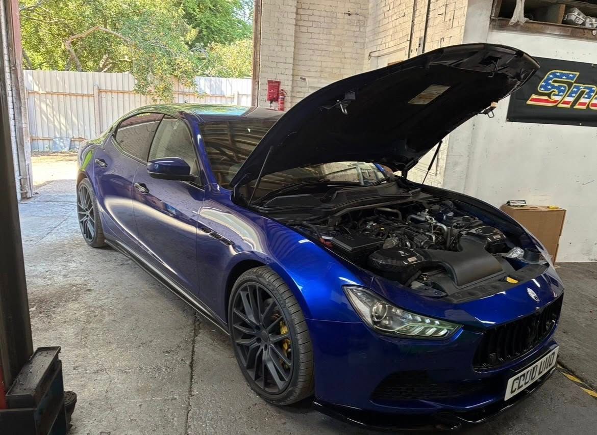 Blue Maserati Ghibli with the hood open in a garage setting.