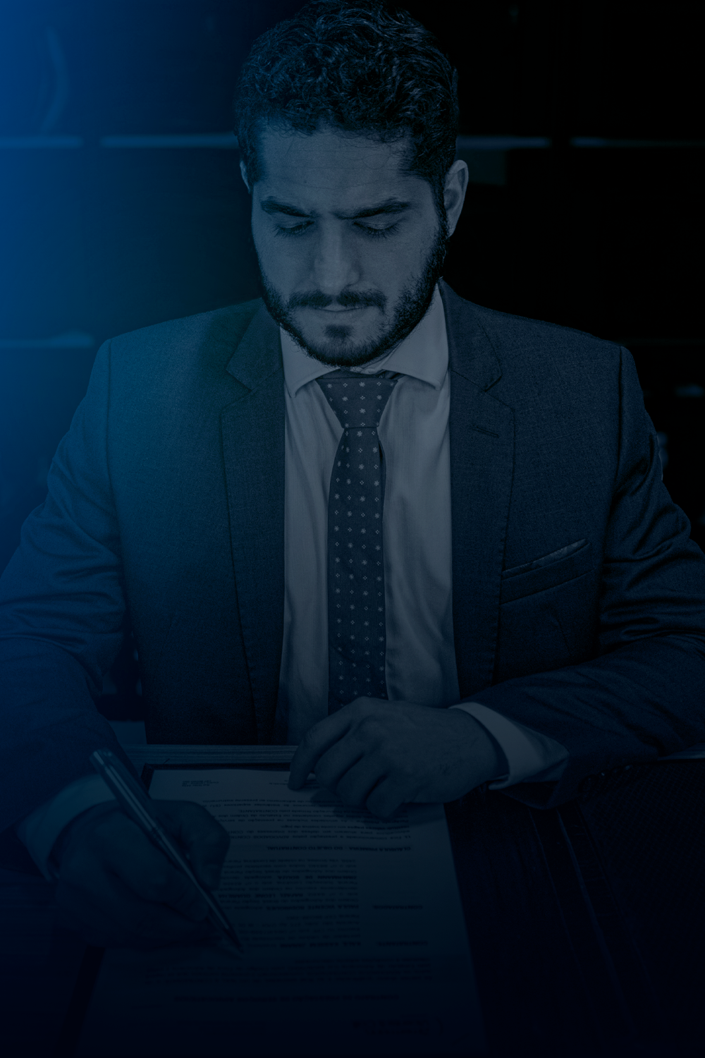 Homem de terno olhando para baixo, escrevendo em um papel sobre uma mesa. Azul escuro, ambiente de negócios.