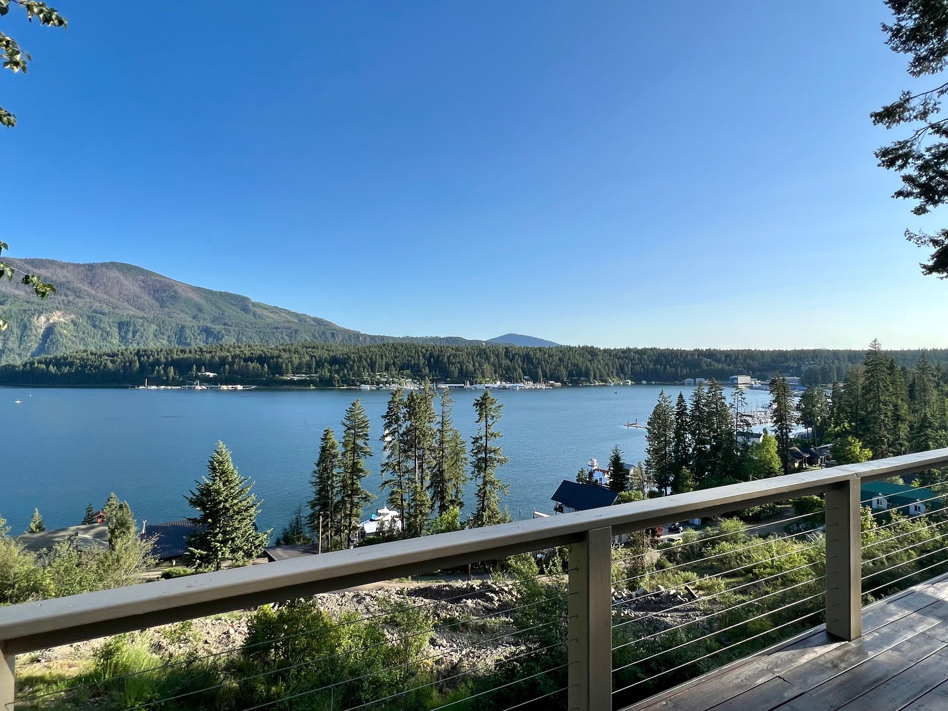 Lake view from a wooden deck. Mountains, blue water, and sky. Trees surround the lake.