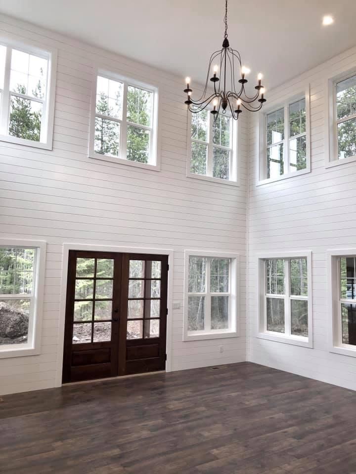 High-ceiling entry with white shiplap walls and natural light from numerous windows. A chandelier hangs from the ceiling.