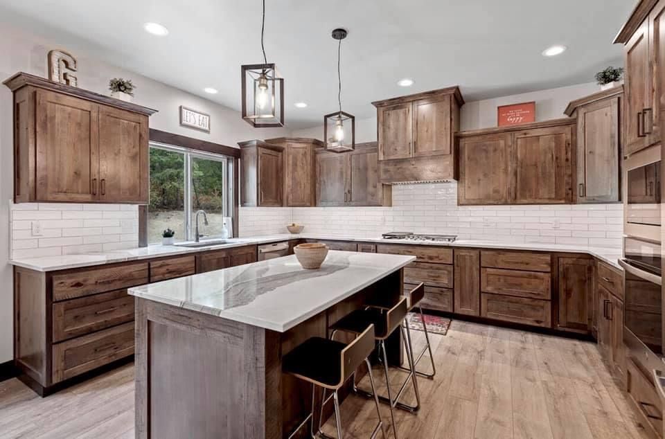 A modern kitchen with wood cabinets, white countertops, island with seating, and pendant lights.