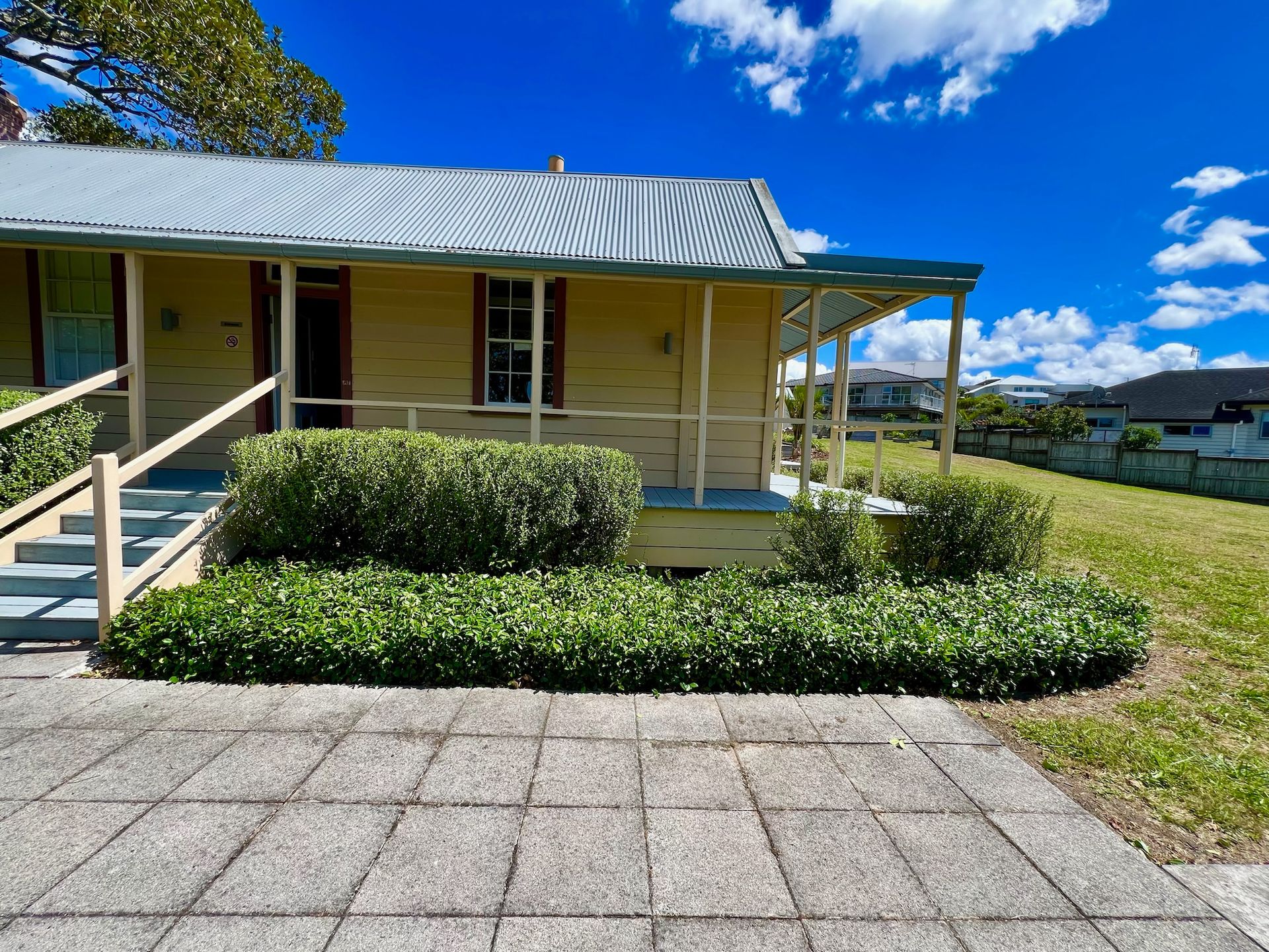 Yellow house with porch, green shrubs, blue sky with clouds.