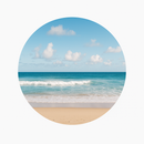Blue ocean waves crashing on a sandy beach under a bright blue sky with clouds.
