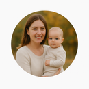 Woman smiling, holding baby, both in light-colored clothes.  Outdoor background, autumn colors.