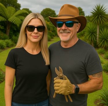 Woman and man in a garden. Man holds pruning shears, wearing a hat and sunglasses. Woman wears sunglasses, smiles.