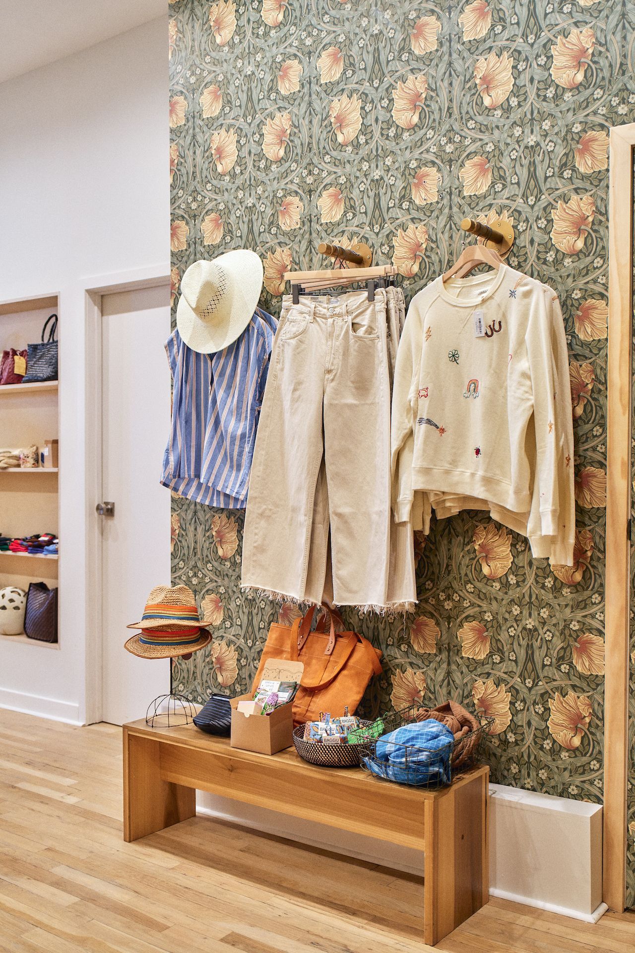 A store with clothes hanging on a wall and a wooden bench.