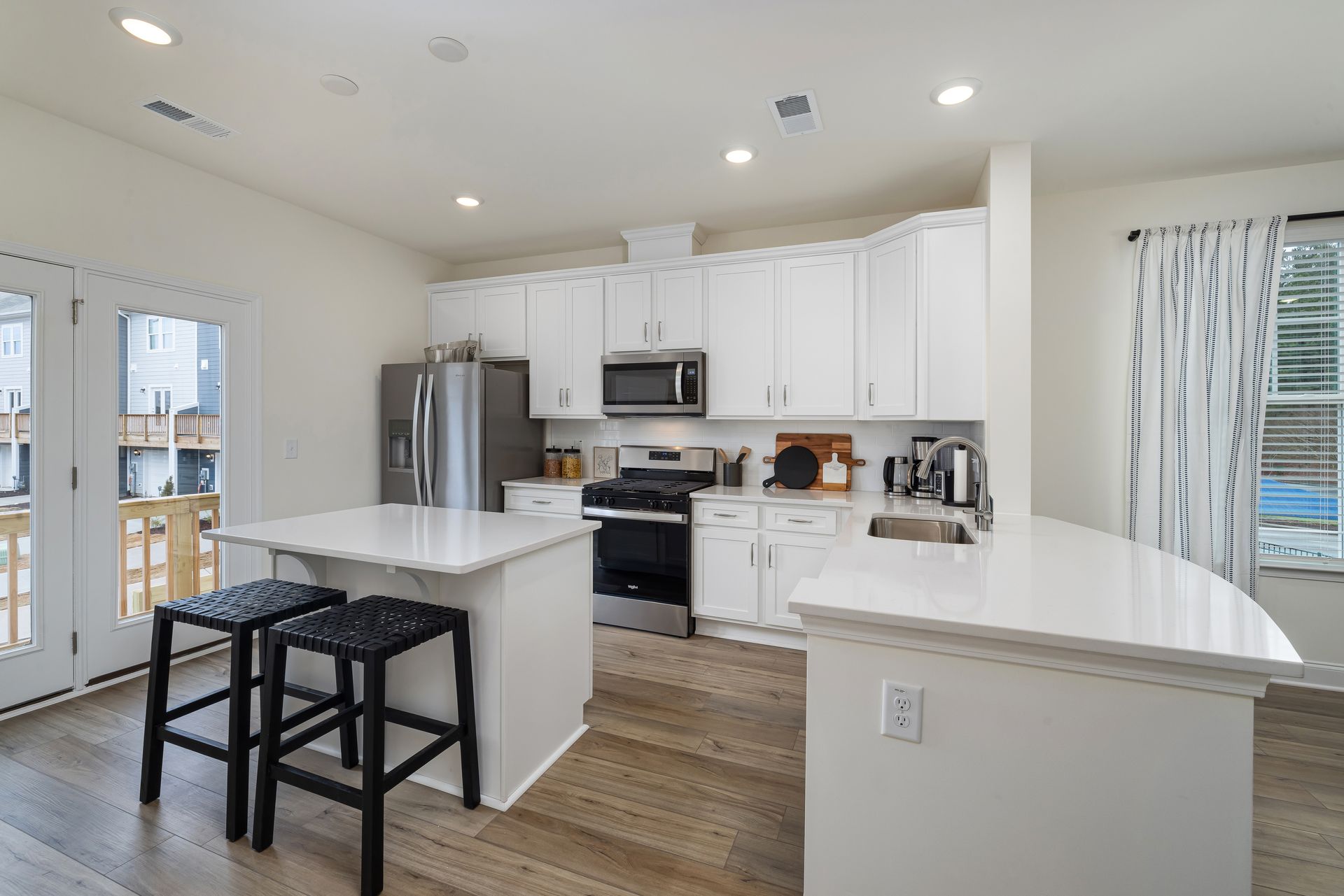 Modern white kitchen with two islands, stainless steel appliances, and wood flooring.