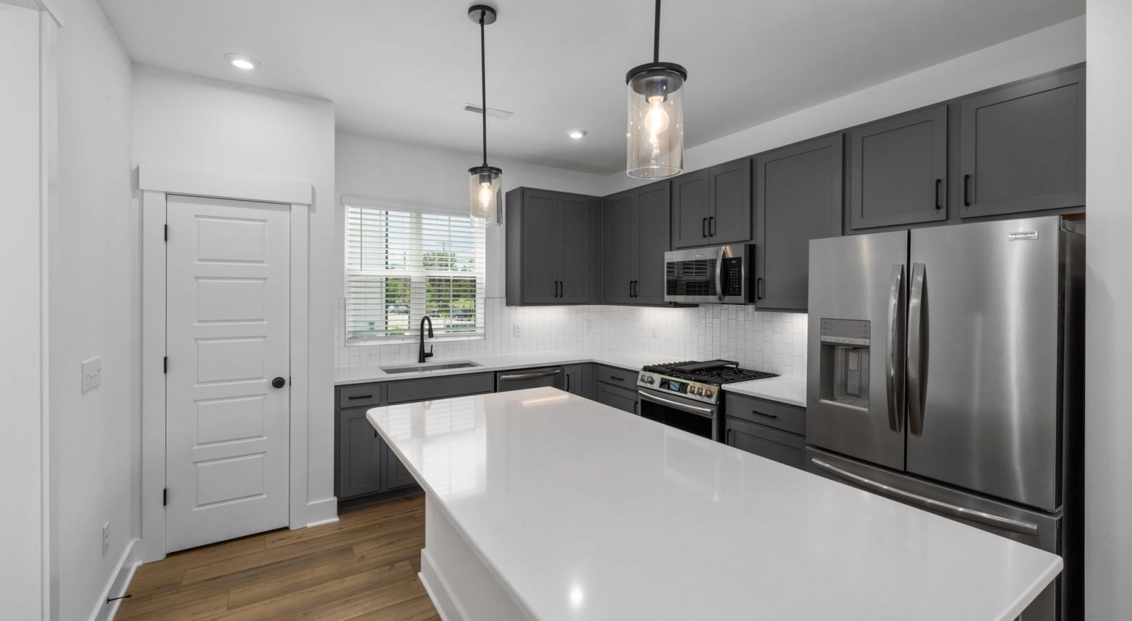 Modern gray kitchen with white countertops, stainless steel appliances, and two hanging lights.