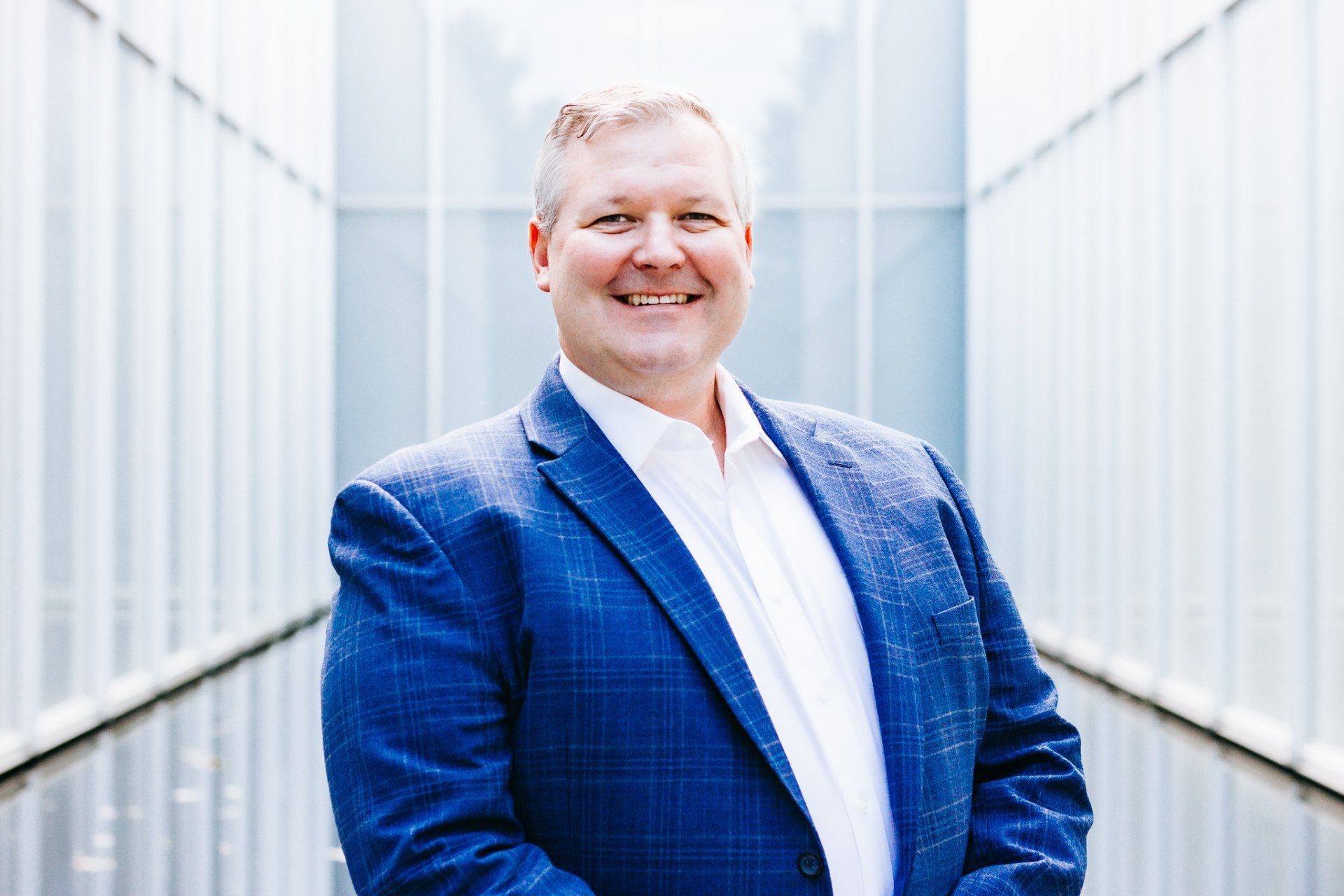 a man in a blue suit and white shirt is standing in front of a building .