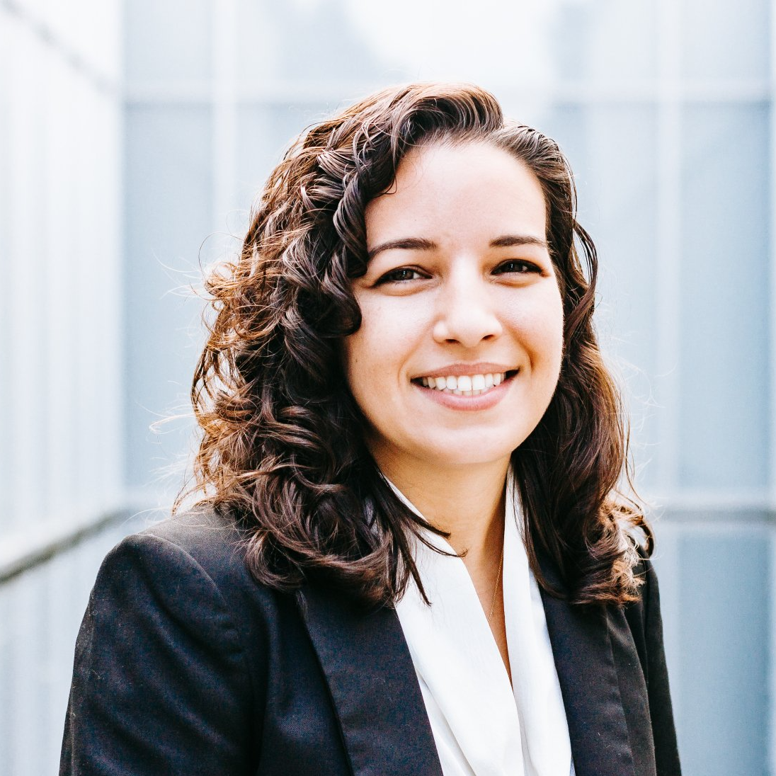 a woman with curly hair wearing a black jacket and white scarf smiles for the camera .