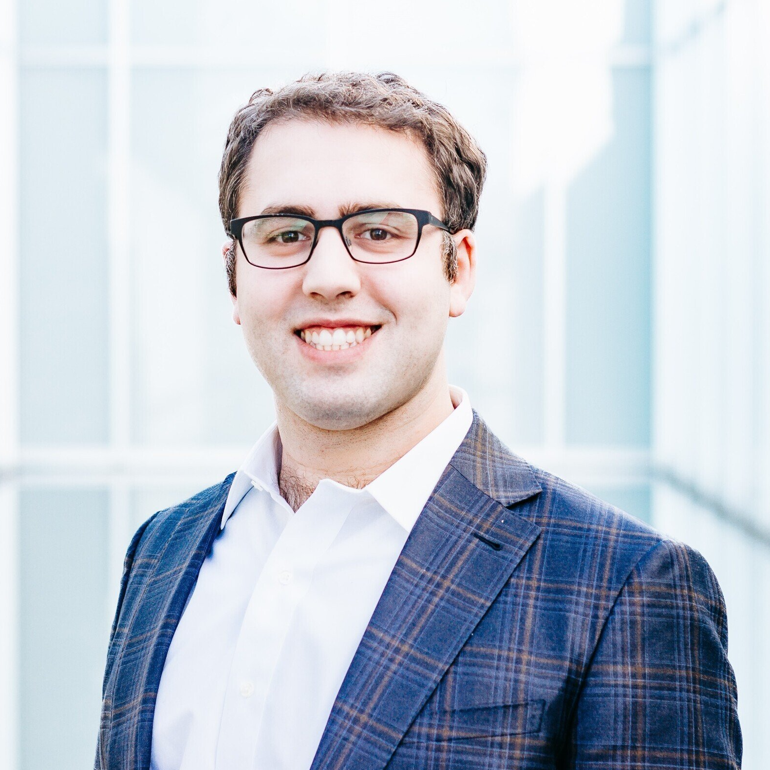 a man wearing glasses and a suit is smiling for the camera .
