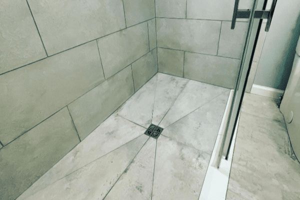 A shower stall with a tiled floor and a glass door in a bathroom.