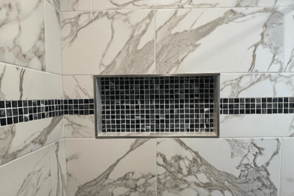 A shower stall with marble tiles and a stainless steel drain.