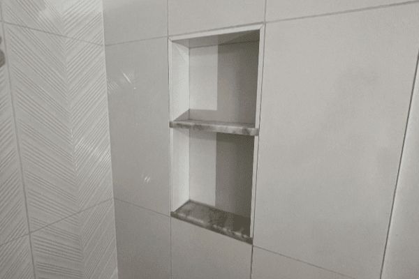 A bathroom with white tiles and a shelf in the wall.