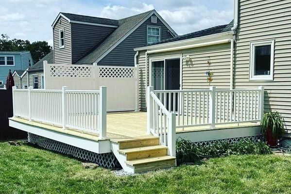A wooden deck with white railing is in the backyard of a house.