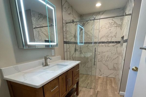 A bathroom with a sink , mirror and walk in shower.