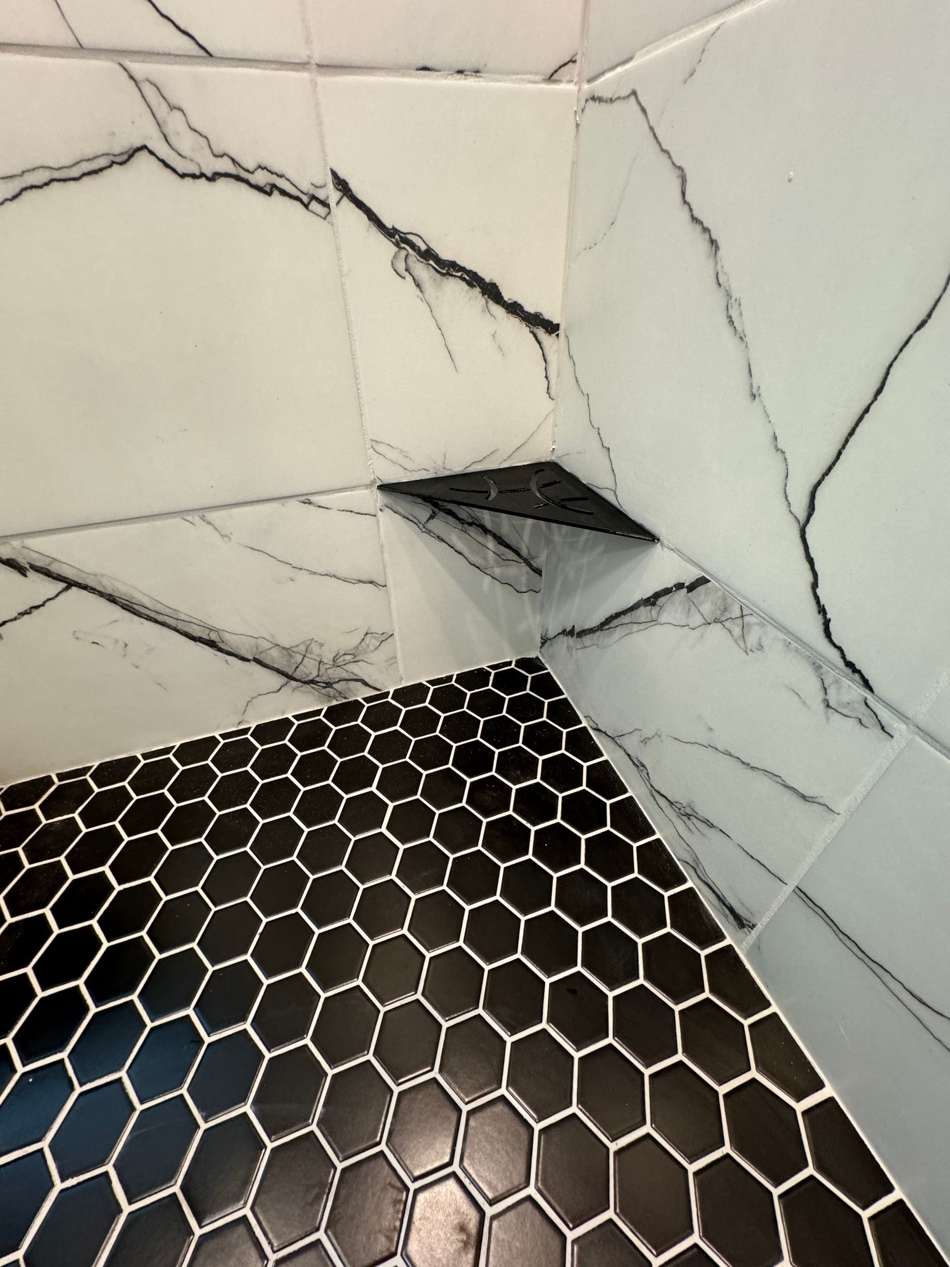 A shower with black and white tiles and a marble wall