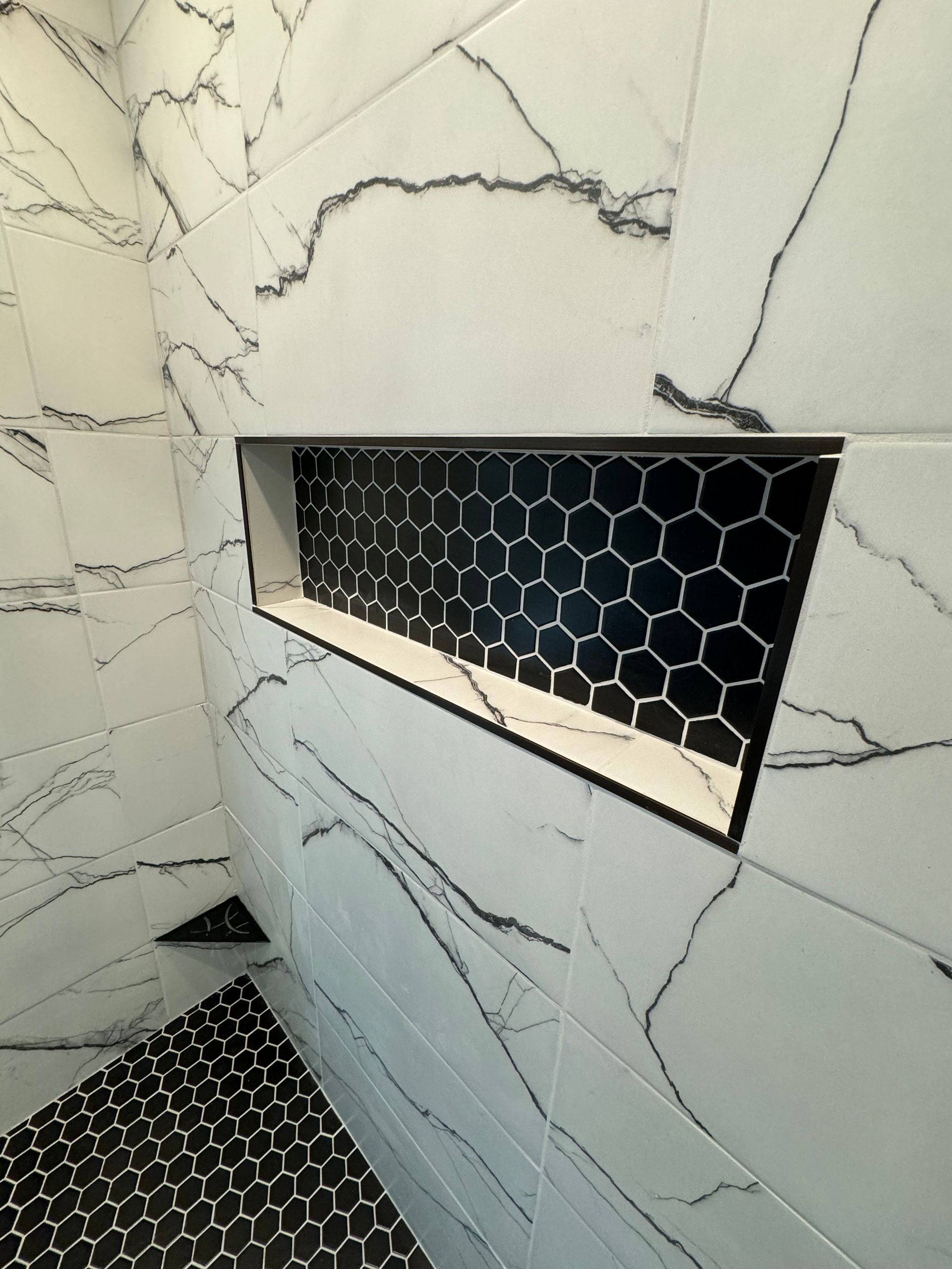 A black and white shower with a honeycomb tile niche
