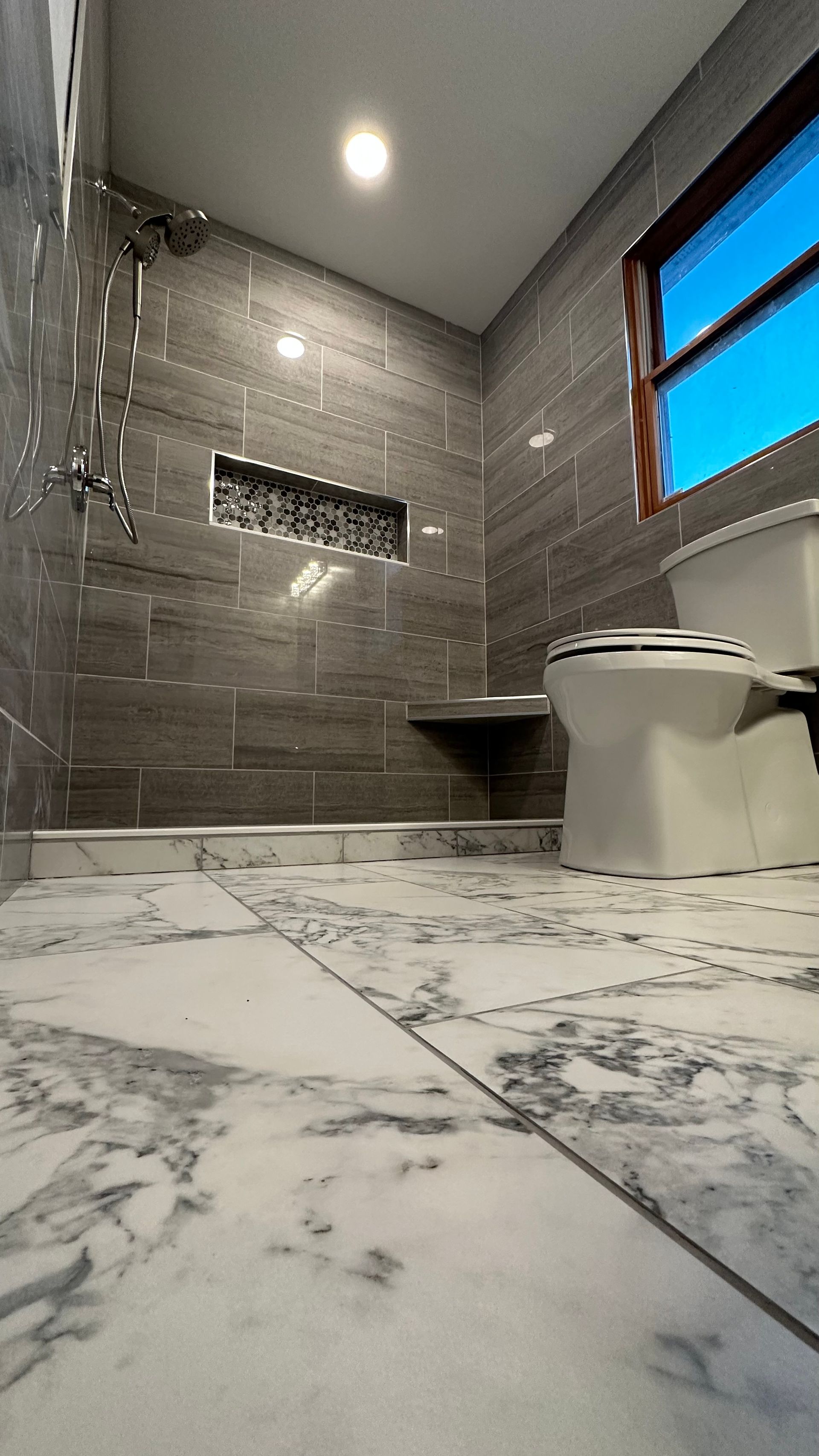 A bathroom with a toilet , shower , and window.