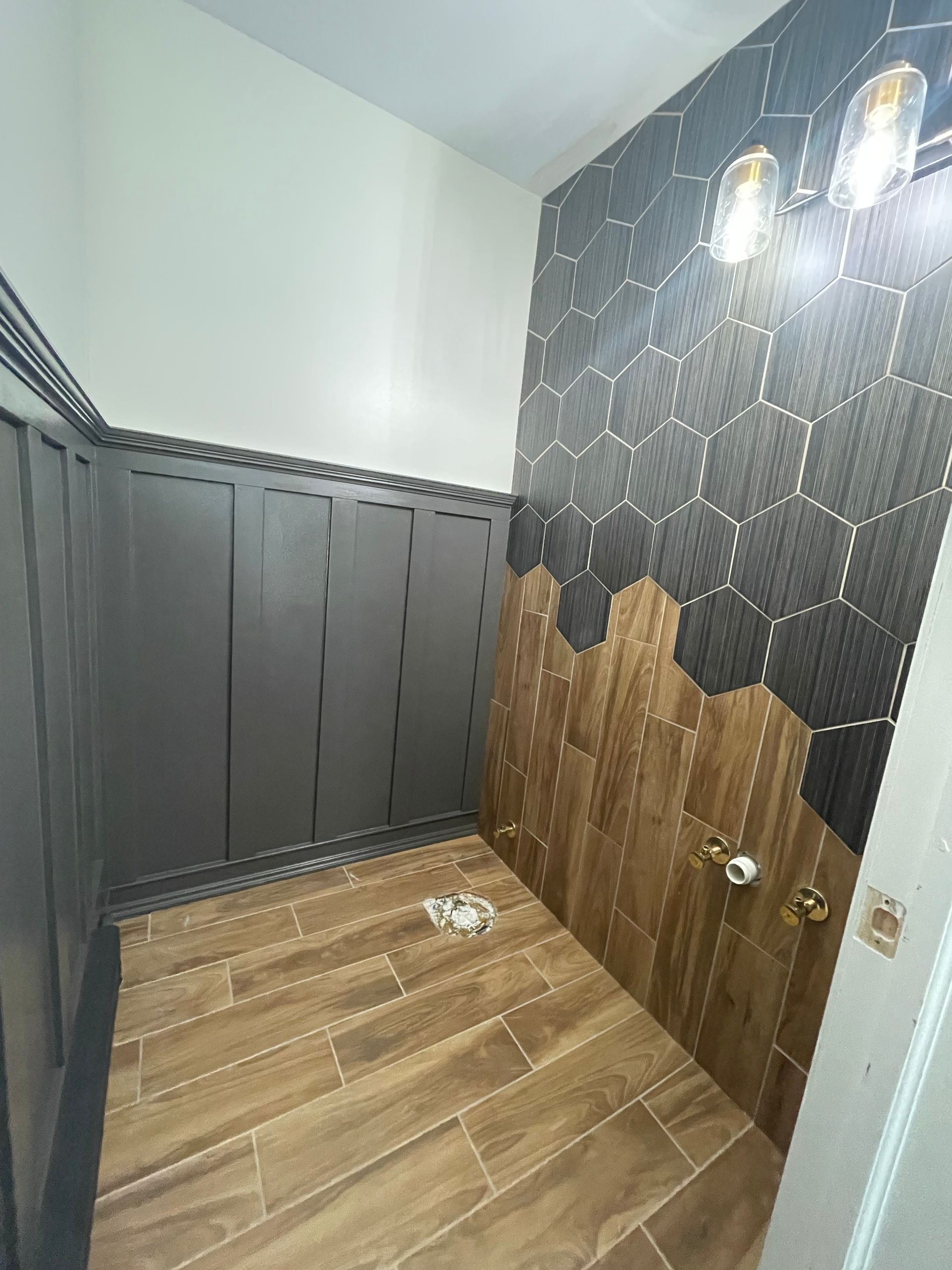 A bathroom with a wooden floor and black tiles on the wall.