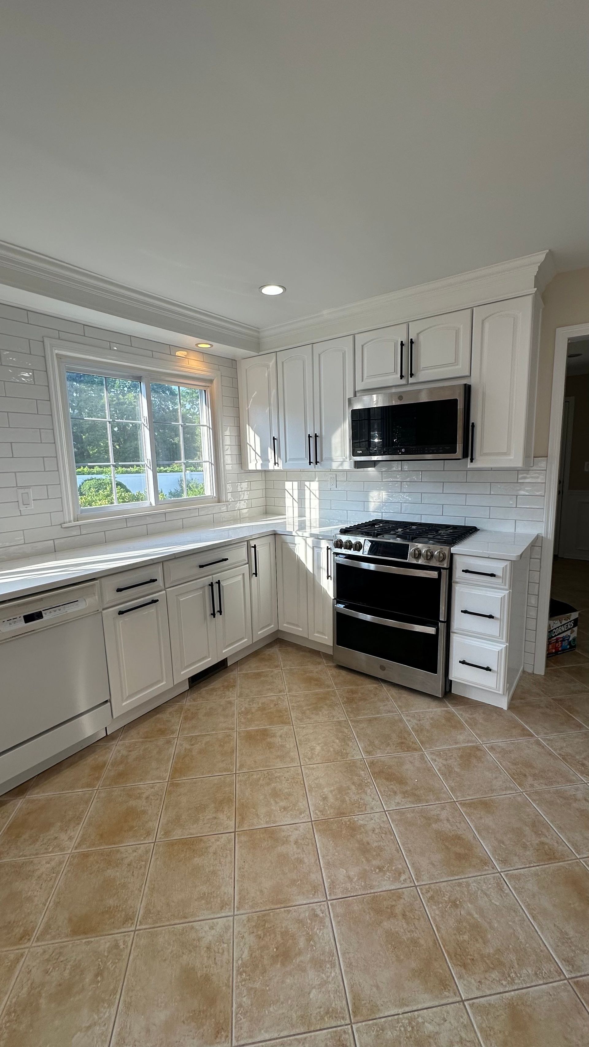 A kitchen with white cabinets , stainless steel appliances , and a large window.