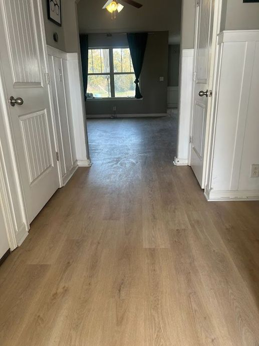 Hallway with light wood-look flooring, white doors, and a window at the end.