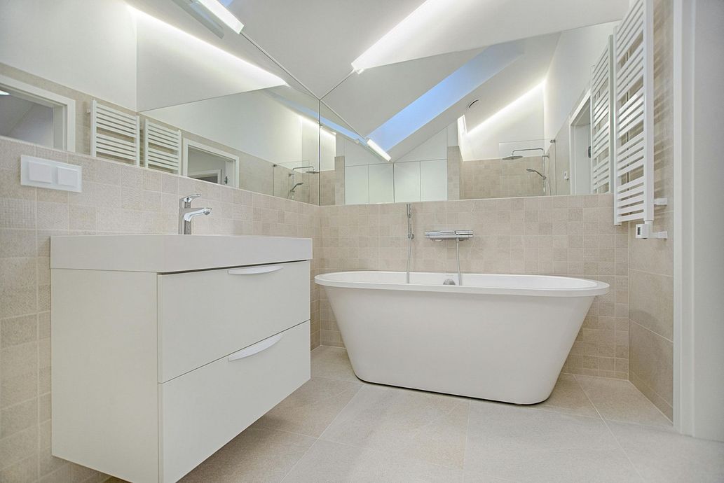 Modern white bathroom with a sink, bathtub, large mirror, and tiled walls.