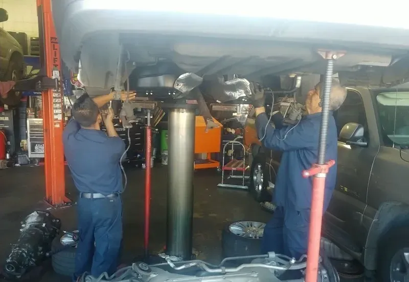 Two mechanics working under a car lifted on a hoist in a garage.