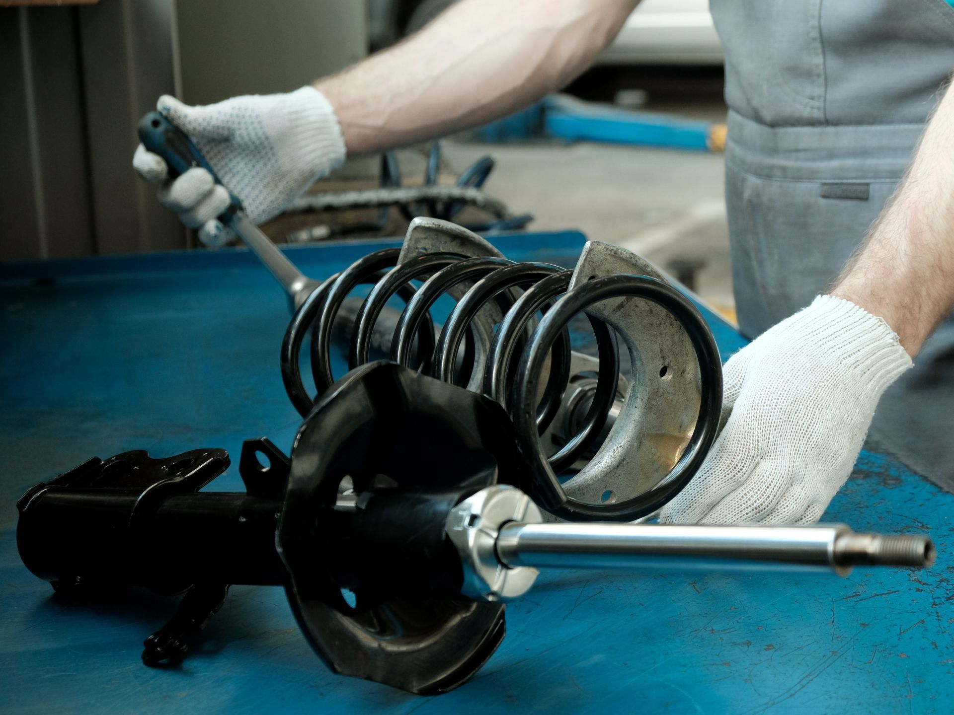 Mechanic holding car suspension parts. A disassembled shock absorber with spring on a blue workbench.