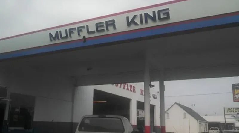 Muffler King shop exterior with white building, red and blue trim, and sign on a cloudy day.